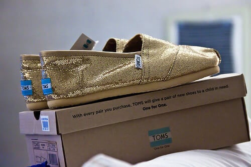 a pair of gold tom’s shoes on top of a shoebox