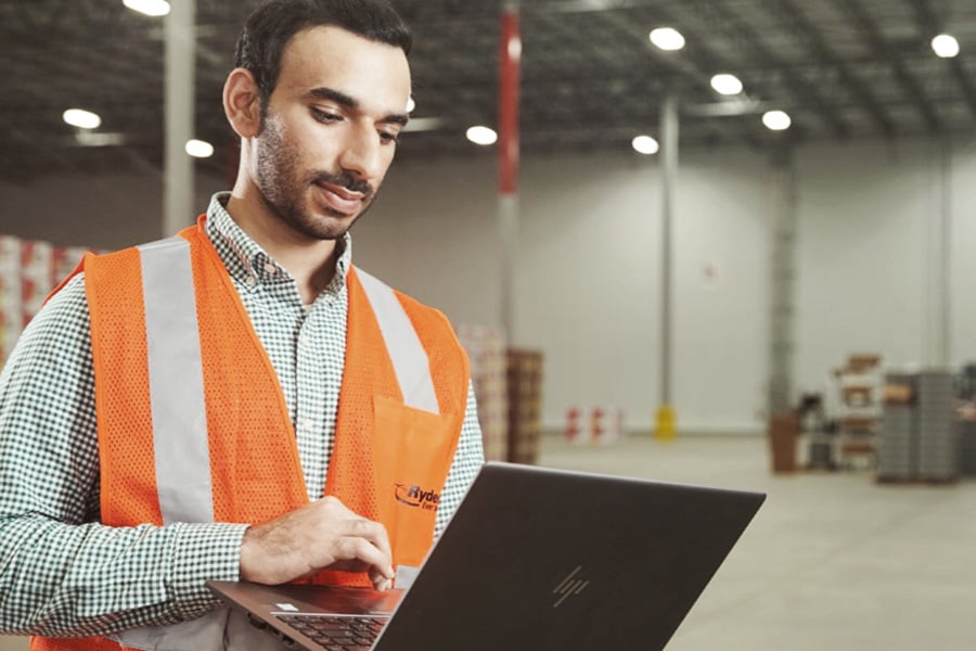 Ryder warehouse employee in a safety vest reviewing current job openings on a laptop Ryder warehouse employee in a safety vest reviewing current job openings on a laptop