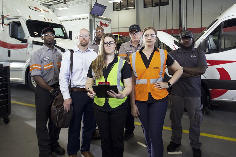 A group of Ryder technicians and staff gathered together in a maintenance shop