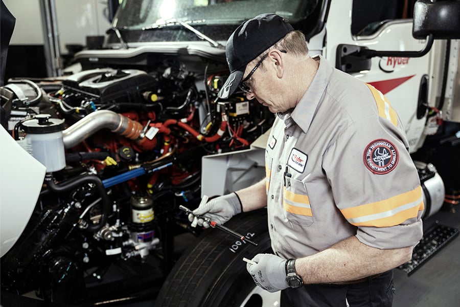 Ryder diesel technician performing maintenance under the hood of a semi truck