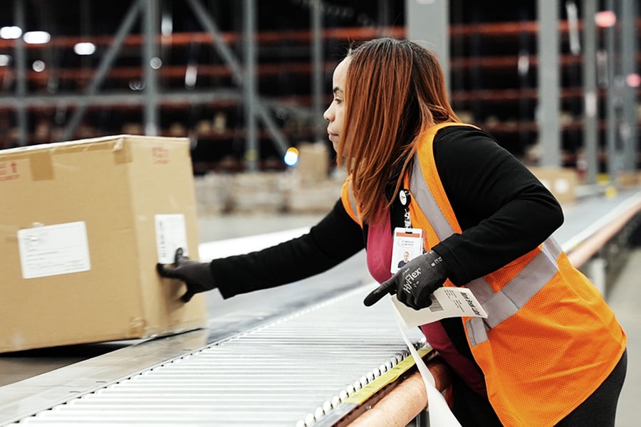 Ryder warehouse worker in a safety vest lifting a box in a distribution center
