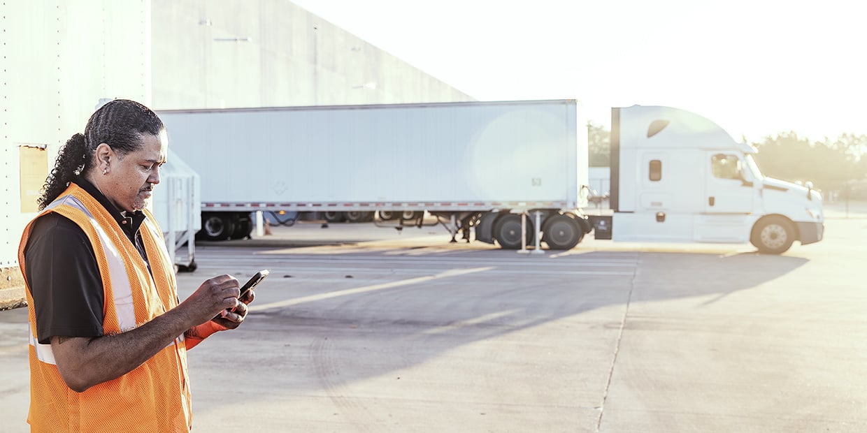 Truck driver using a mobile device near a semi-truck at a loading facility