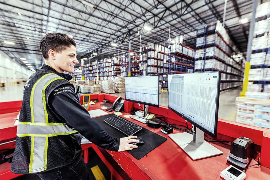Ryder warehouse employee in a safety vest monitoring food and beverage inventory on a screen Ryder warehouse employee in a safety vest monitoring food and beverage inventory on a screen