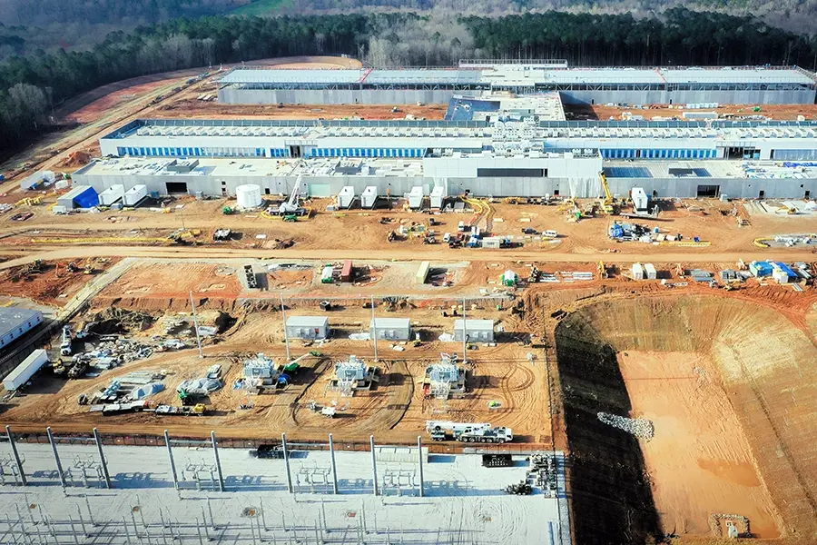Data center construction site with buildings under development and construction equipment on cleared landAerial view of a completed data center facility with rooftop cooling units