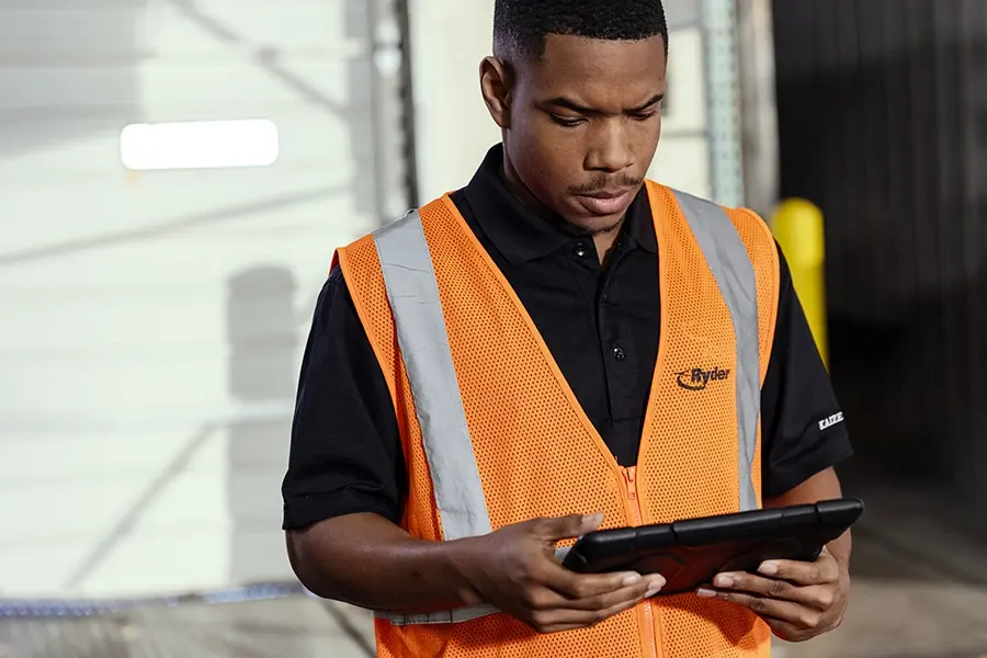 Ryder worker in a safety vest reviewing construction schedules on a tablet at a job site