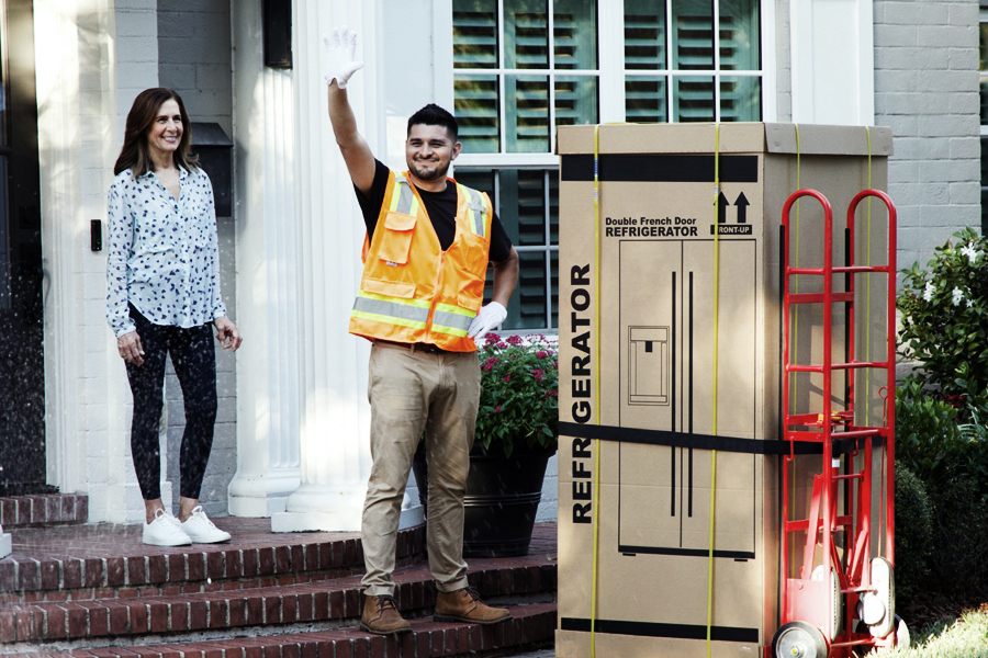 White glove delivery technician unloading a boxed refrigerator at a customer’s home