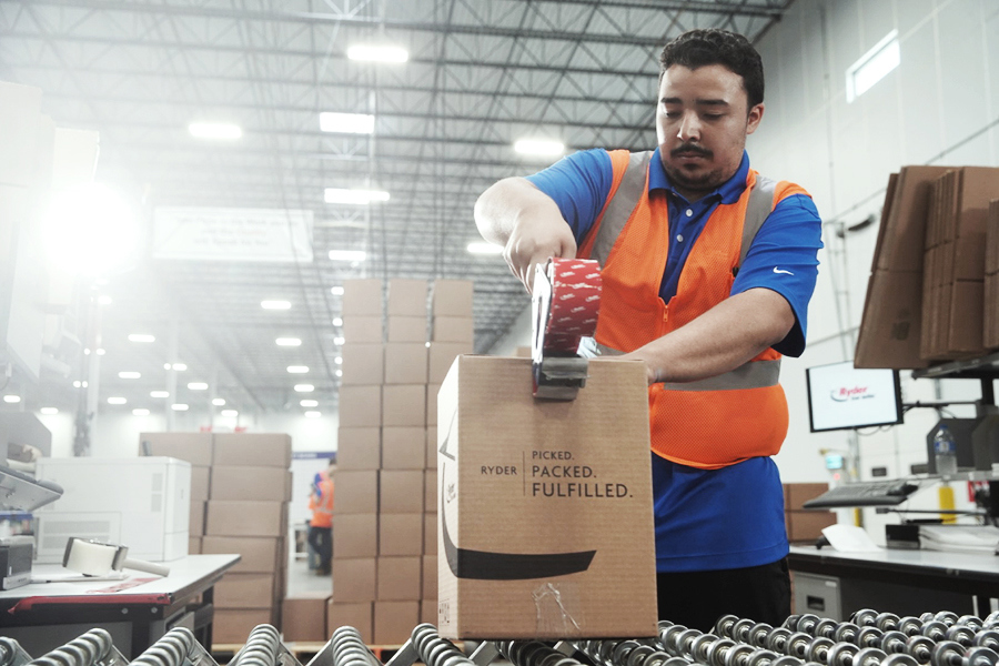 Warehouse worker packing and sealing a shipping box on a fulfillment line