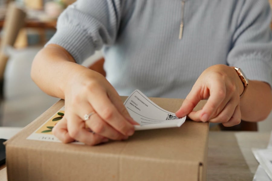 Person putting a shipping label on the box of an e-commerce order Person putting a shipping label on the box of an e-commerce order