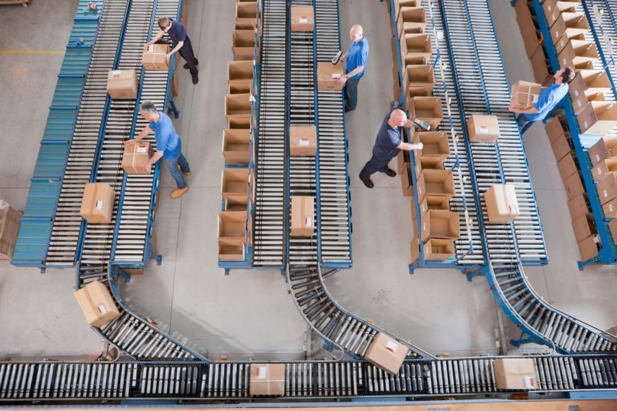 Does Your 3PL Have What It Takes to Support Your Company’s Future Growth? warehouse workers fulfilling orders as parcels roll on conveyance systems.